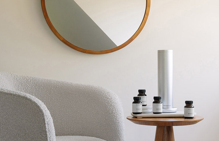 Indoor scene with a table displaying bottles labeled 'Aromatech' and an Aromamini BT Plus diffuser.